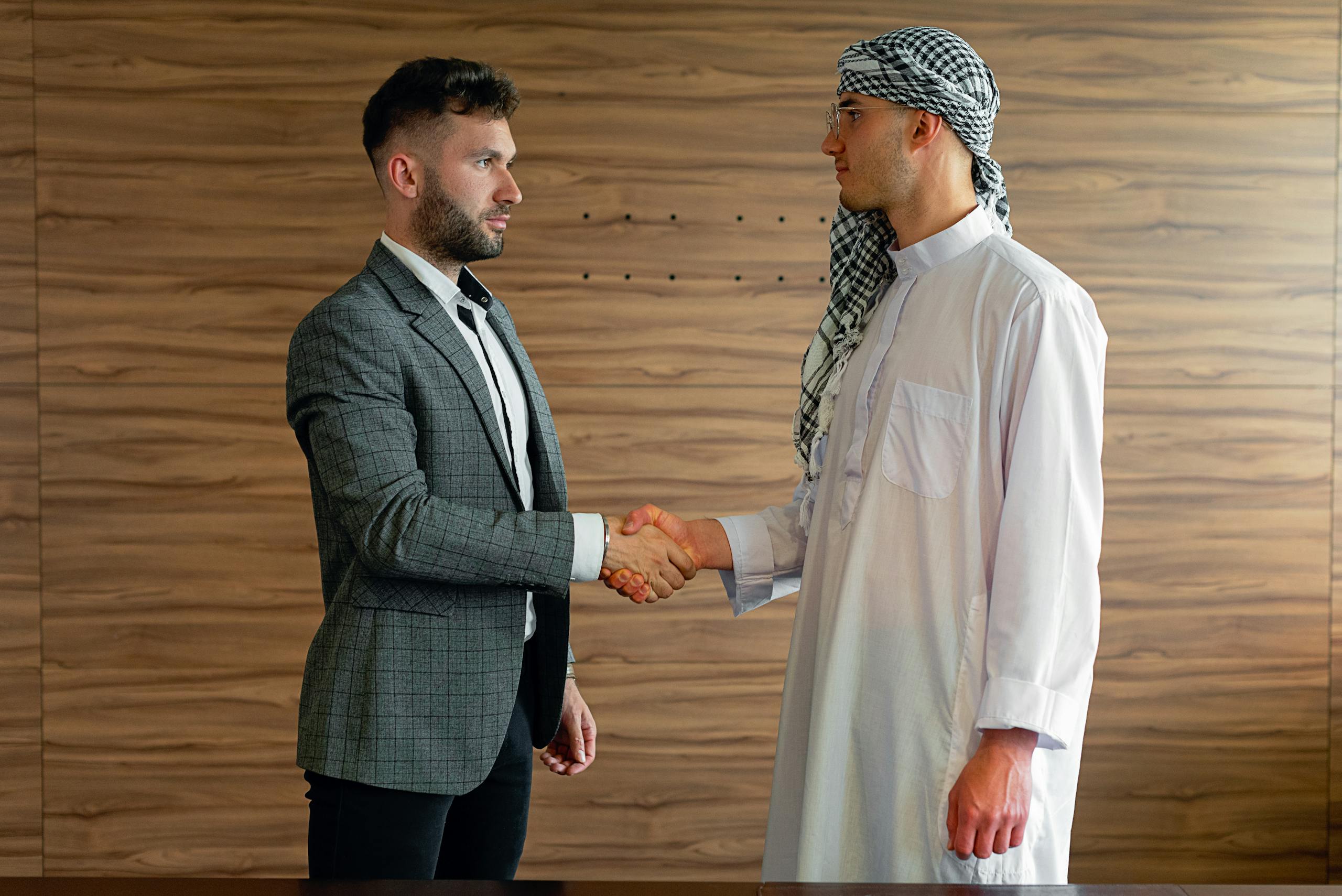 Two businessmen shaking hands indoors, symbolizing a successful cross-cultural partnership.